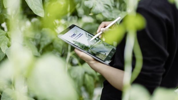 Eine Frau steht mit einem Tablet im Grünen.