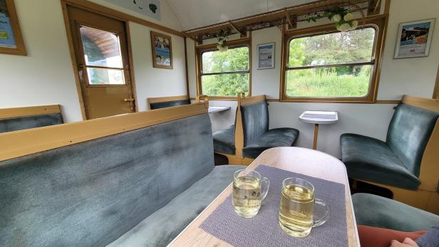 Ein Speisewagen in einem Zug; vorne im Bild ist ein Tisch mit zwei Gläsern Weißwein zu sehen.