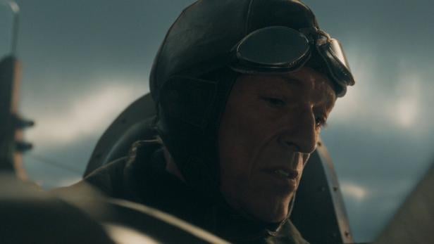 Ein Pilot mit Fliegerhaube und Brille im Cockpit eines Flugzeugs.