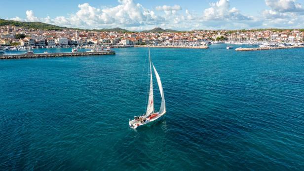 Luftaufnahme eines Segelbootes im Meer mit der Stadt Vodice im Hintergrund.