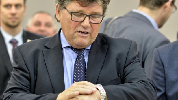 Ein Mann im Anzug blickt auf seine Armbanduhr.
