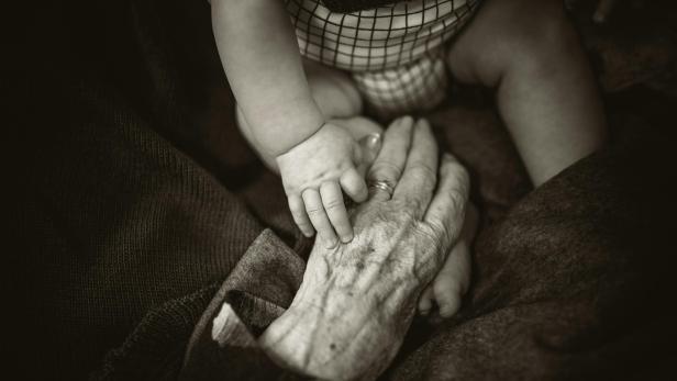 Hand einer alten Frau liegt unter der hand eines Babys