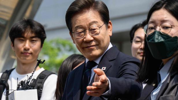 Ein Mann in Anzug mit einer Anstecknadel der südkoreanischen Flagge streckt seine Hand aus.