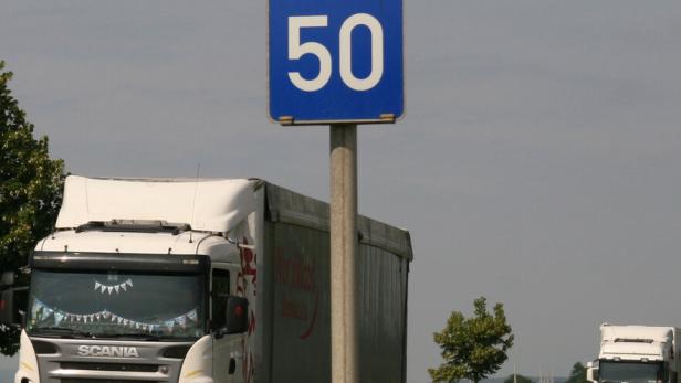 Straßenschild mit Vorfahrt und Tempo 50, daneben zwei Lastwagen auf einer Landstraße.