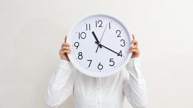 Businesswoman holding a clock against wall