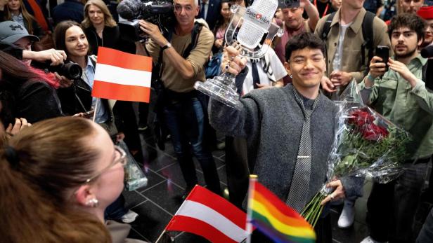 Nemo, der Gewinner des Eurovision Song Contest, hält die Trophäe in die Höhe, umringt von Fans mit österreichischen und Regenbogenflaggen.