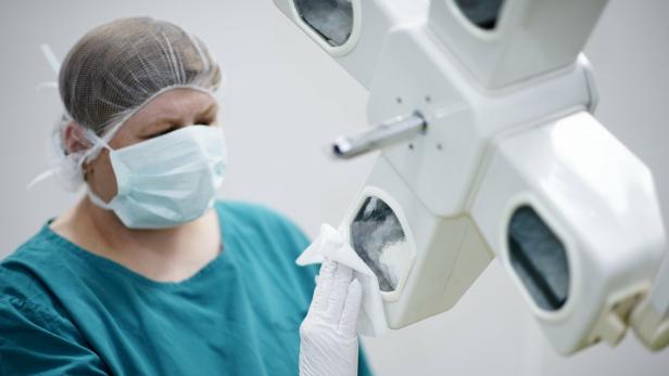 Eine Frau in einem OP-Mundschutz und Scrub-Anzug hält ein chirurgisches Licht.