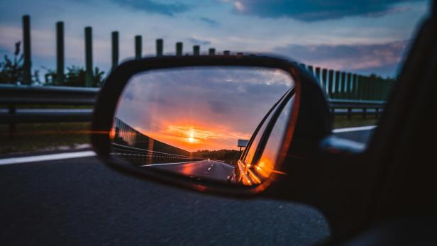 Im Seitenspiegel eines Autos ist der Sonnenuntergang zu sehen