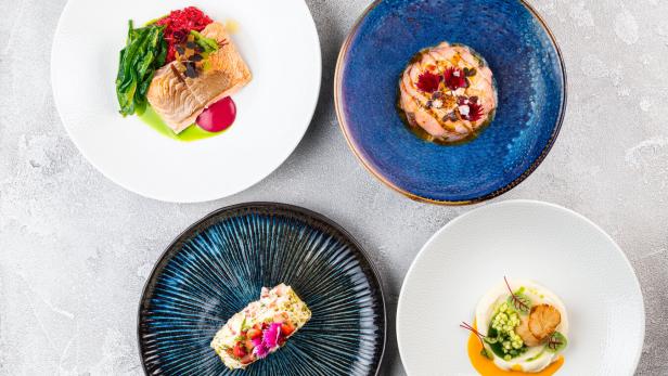 Vier Teller mit kunstvoll angerichteten Speisen, darunter Fisch und Meeresfrüchte.