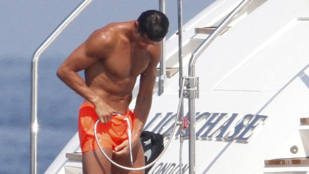 Ein Mann mit orangefarbener Badehose duscht auf einer Yacht.
