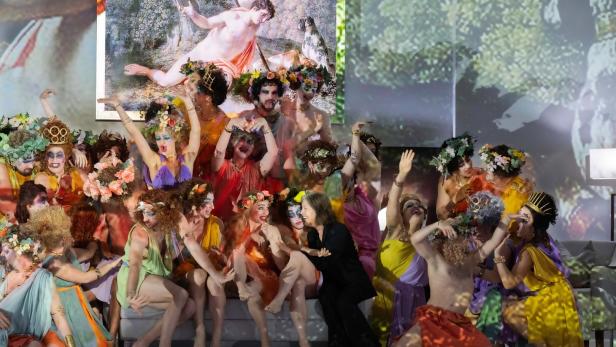 Eine Gruppe von als griechische Gottheiten verkleideten Menschen posiert auf einer Bühne.