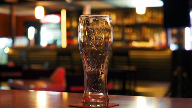 Empty beer glass on the table in a dark evening bar, panoramic view