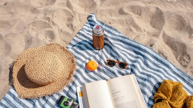 Ein Strandtuch mit einem Sonnenhut, einem Buch, einer Kamera und einer Sonnenbrille, am Strand