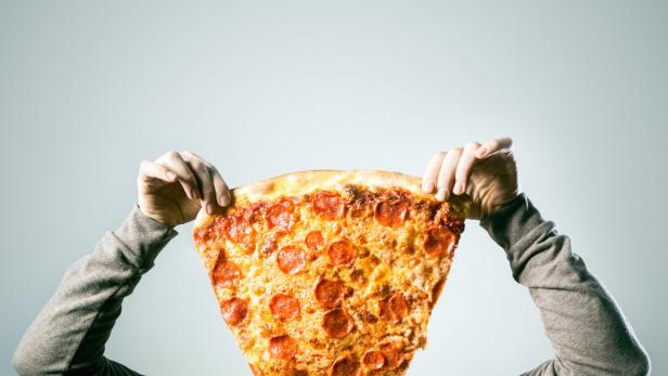 Mann hält eine riesige Pizzaschnitte vor sein Gesicht