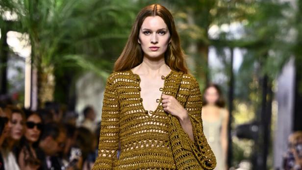 Ein Model läuft auf dem Laufsteg in einem gehäkelten Minikleid mit passender Tasche.