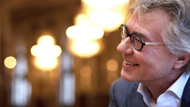 Ein lächelnder Mann mit Brille im Profil vor verschwommenen Lichtern.