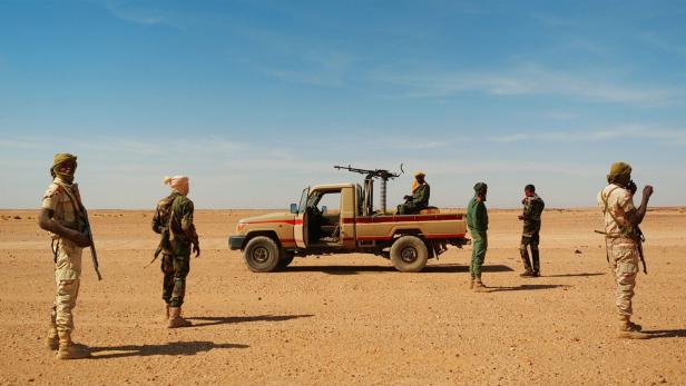 Eine Gruppe bewaffneter Soldaten steht in der Wüste neben einem Militärfahrzeug mit montiertem Maschinengewehr.