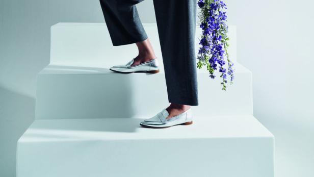 Eine Frau in weißem Hemd und grauer Hose steigt mit einem Blumenstrauß eine weiße Treppe hinauf.