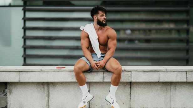 Ein muskulöser Mann entspannt sich nach dem Training im Stadtpark.