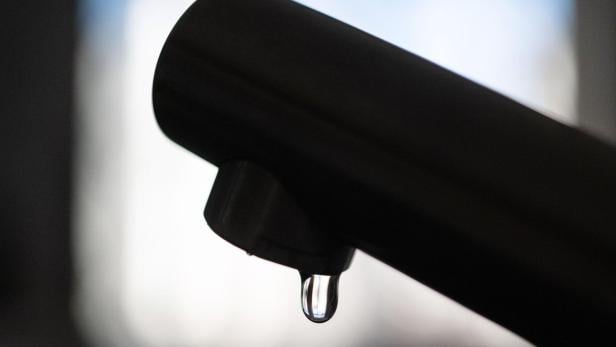 Ein Tropfen hängt an einem dunklen Wasserhahn.