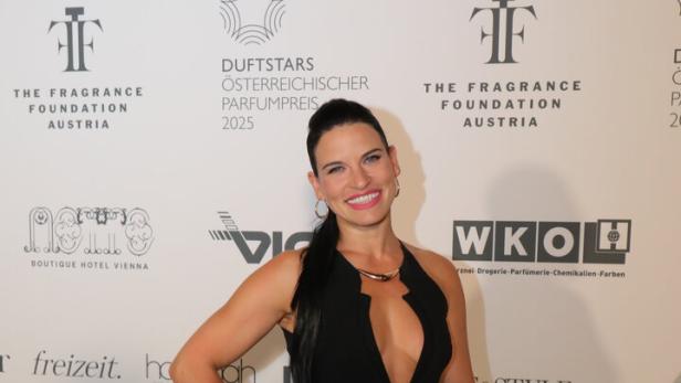 Eine Frau in Abendgarderobe posiert vor einer Wand mit Sponsorenlogos.