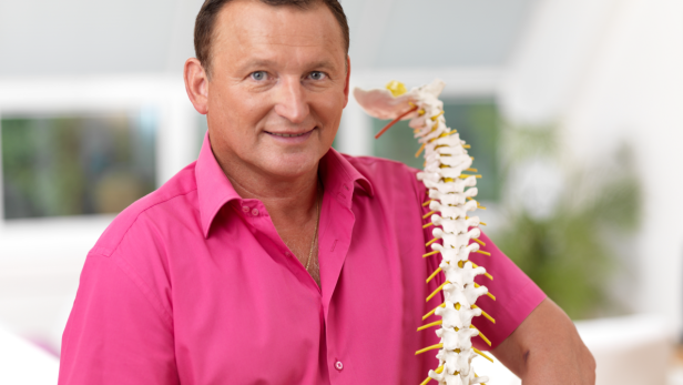 Ein Mann in einem pinken Hemd mit einem Rückenmarkknochen im Arm. 