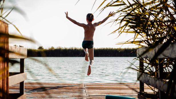 Young boy having fun enjoying a summer day jumping at the lake.