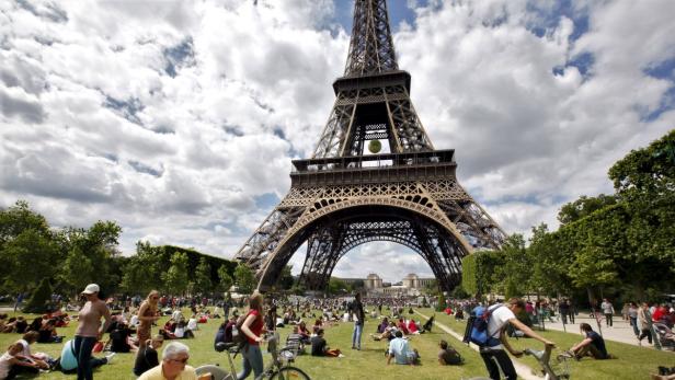 Menschen entspannen auf einer Wiese vor dem Eiffelturm in Paris.
