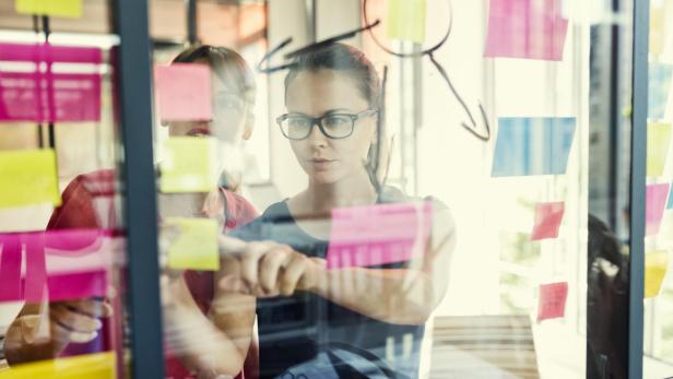 Two business women working together on wall glass