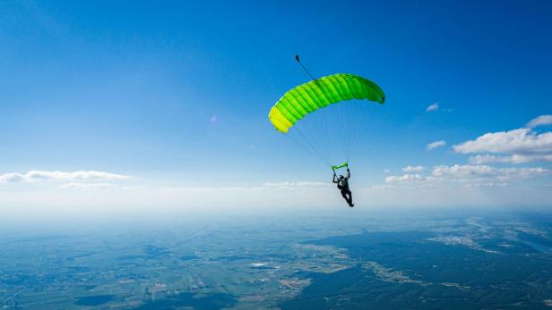 Ein Fallschirmspringer schwebt mit einem gelb-grünen Fallschirm über einer Landschaft.