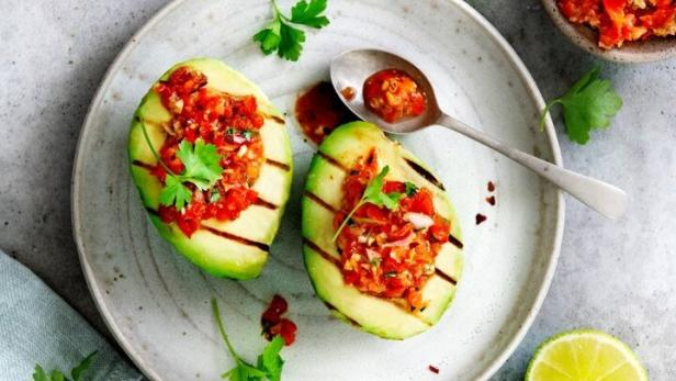 Zwei gegrillte Avocadohälften gefüllt mit Tomatensalsa auf einem Teller.