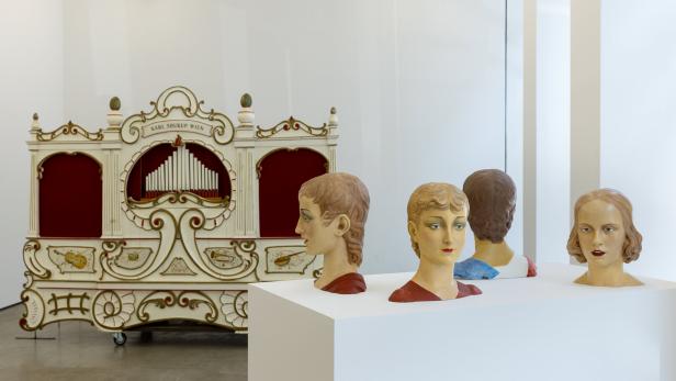 Eine Drehorgel von Karl Soukup Wien und drei Büsten in einer Ausstellung.