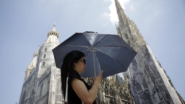 A tourist holds an umbrella in front of St. Stephens cathedral on a sunny day in Vienna