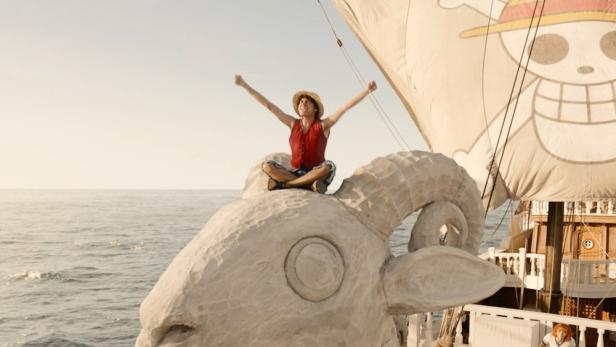 Ein Mann im Strohhut sitzt auf dem Bug des Schiffs aus der Serie „One Piece“ und jubelt.