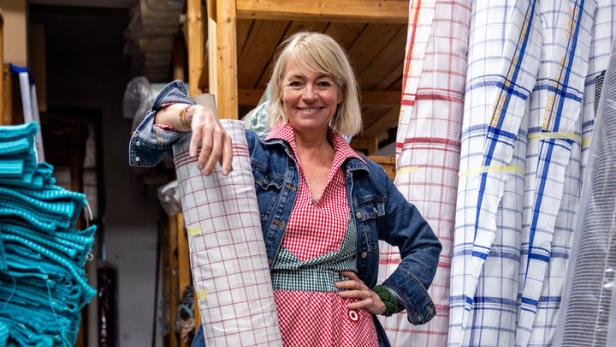 Eine Frau in einem rot-weiß karierten Kleid posiert mit Stoffrollen in einem Lager.