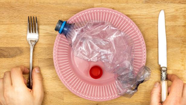 Microplastic in food, Concept, Global environmental problem, Plastic Pet bottle on a plate, hands reaching for a knife and fork, microplastics and pollution entering the body