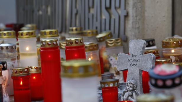 Kerzen und ein Kreuz mit der Aufschrift „Wir vermissen Dich“ vor einem Schulgebäude.
