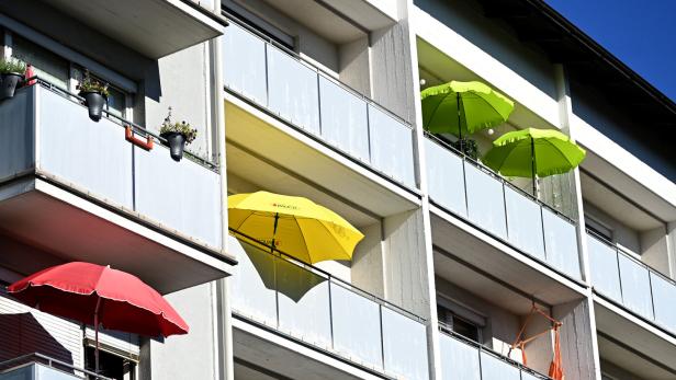 Bunte Sonnenschirme stehen auf den Balkonen eines Wohnhauses.