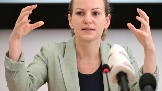 Eine Frau gestikuliert während einer Pressekonferenz vor mehreren Mikrofonen.