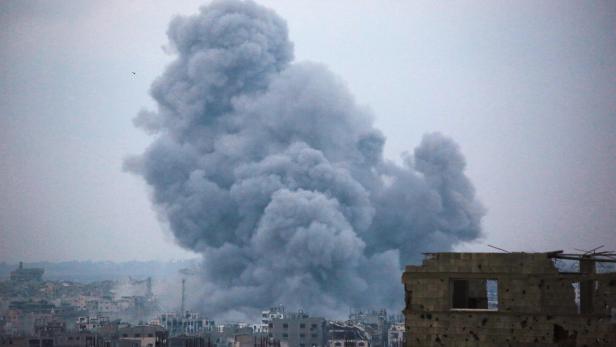 Eine große Rauchsäule steigt über zerstörten Gebäuden in einer Stadt auf.