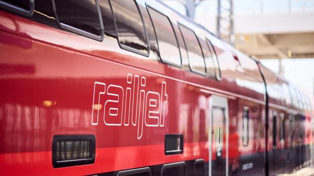 Ein roter Railjet-Zug steht an einem Bahnhof.