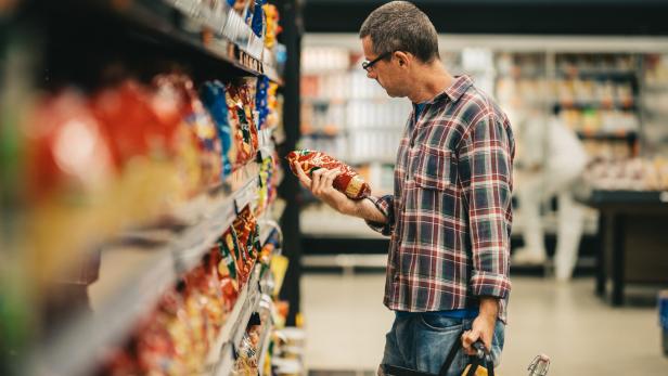 Man reading a label while grocery shopping in a supermarket aisle