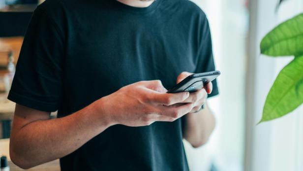 Der 25-jährige Bradley Hall arbeitete im Ausland als Lehrer. Doch im Mai verstarb er plötzlich nach einem Telefonat mit seiner Mama. Mann in schwarzem Shirt hält Handy in der Hand