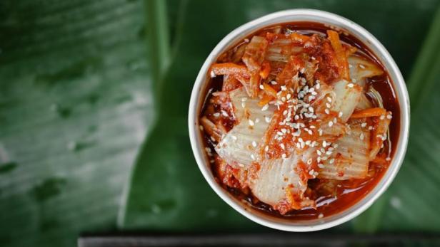 Fermentiertes Kimchi in einer Schale auf Bananenblättern mit Sesamsamen garniert – traditionelles koreanisches Fermentationsgericht reich an Probiotika.