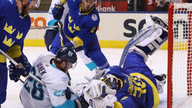 Ein Eishockeyspieler in Blau versucht, den Puck am Torwart vorbei ins Tor zu schießen.