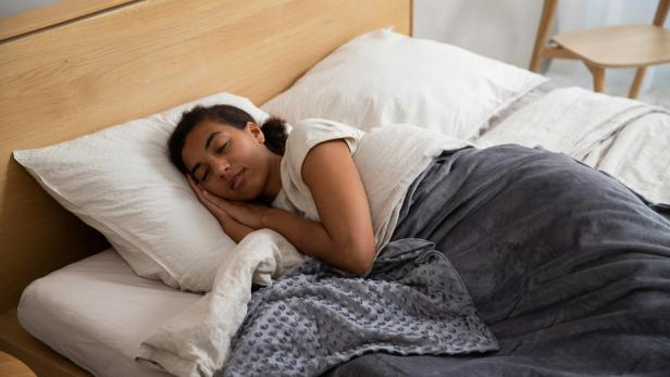 Eine schlafende Frau liegt im Bett, umgeben von weichen Kissen und warmen Decken.