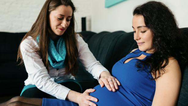 Eine Frau berührt mit ihren Händen den Babybauch einer schwangeren Frau.