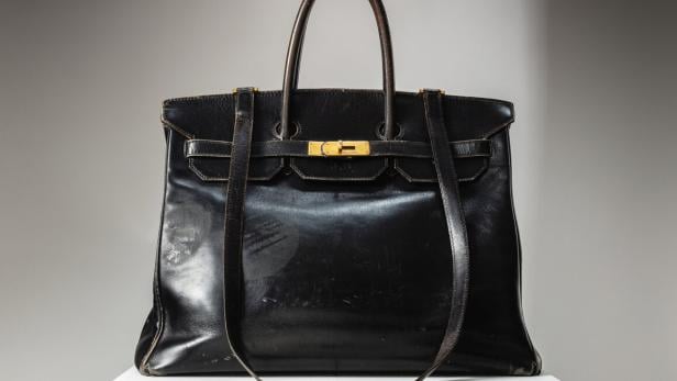 Eine schwarze Birkin Bag von Hermès steht auf einem weißen Sockel.