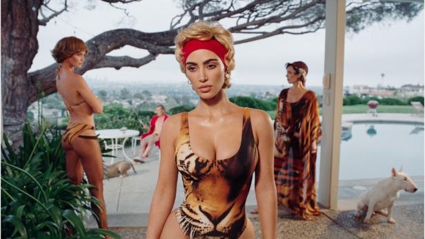 Eine Frau in einem Tiger-Badeanzug posiert mit anderen Models und Hunden an einem Pool.