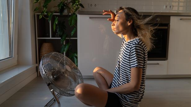 Exhausted woman refreshing sit near big indoor ventilator blowing cooling fresh air at home on floor